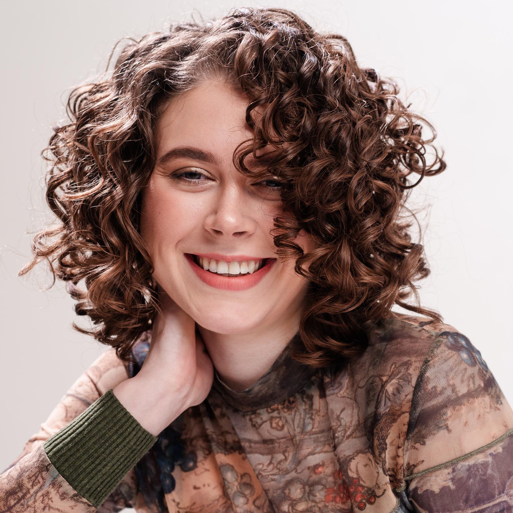 Frau mit kurzen, braunen Locken lächelt entspannt in die Kamera