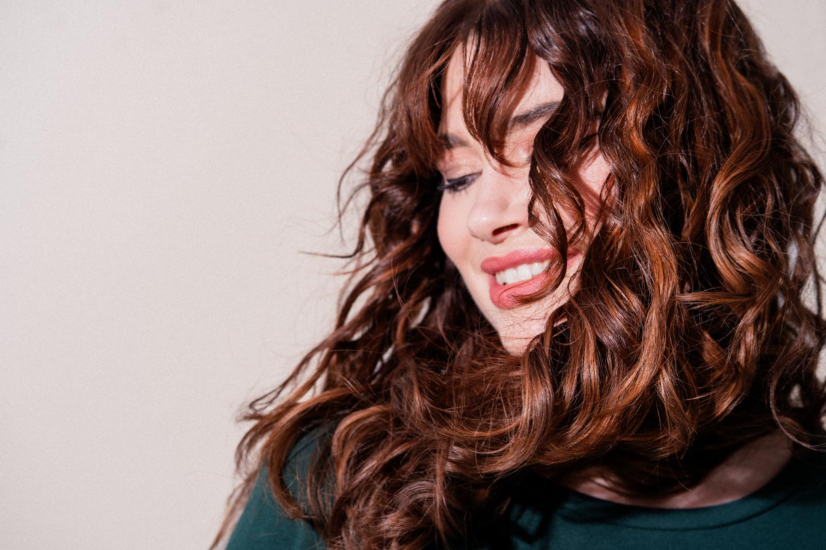 Porträt einer Frau mit langen, braunen Locken und sanfter Bewegung im Haar